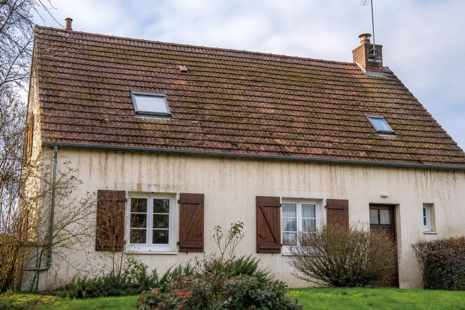 Maison avec toiture en tuiles moussue et façade marquée avant entretien